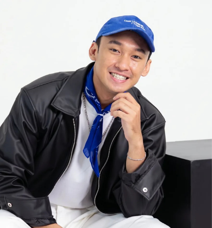 Portrait of Leonaldo, smiling in a blue cap, black leather jacket and blue bandana, resting his chin on his hand