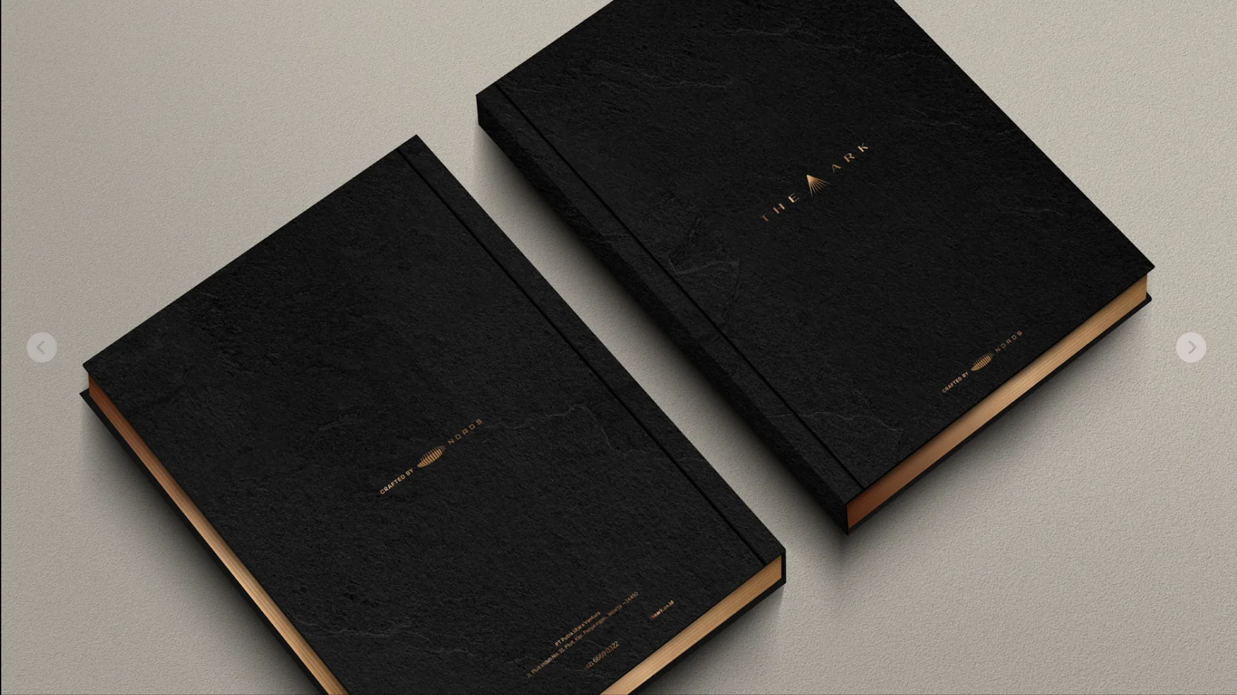 Two black The Ark brochures with a copper edge on a beige surface