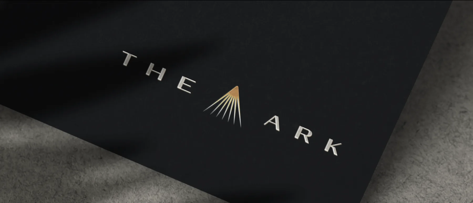 The Ark logo, with copper rays between the words, on black material