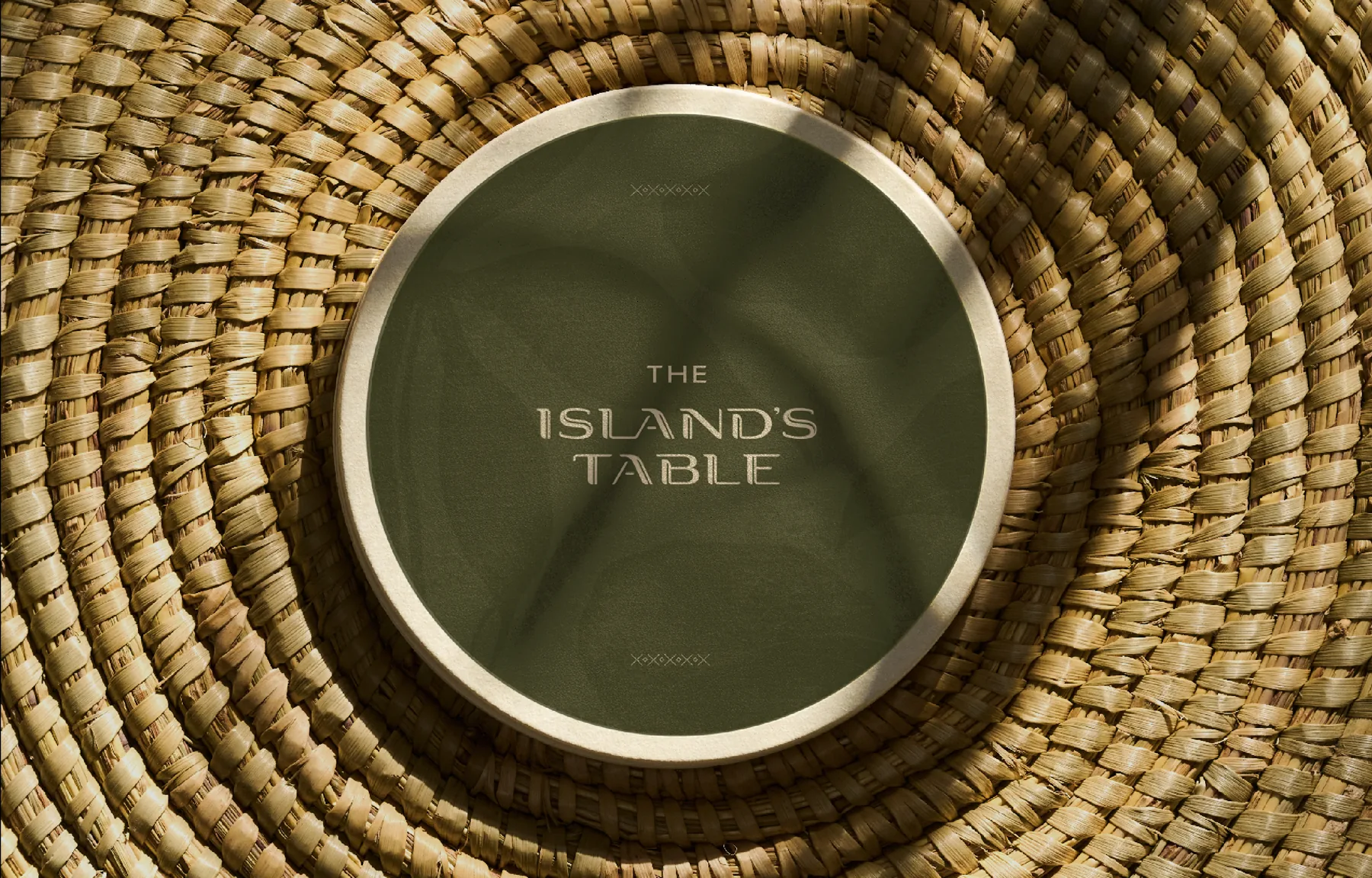 Round plate with The Island’s Table wordmark on woven rattan