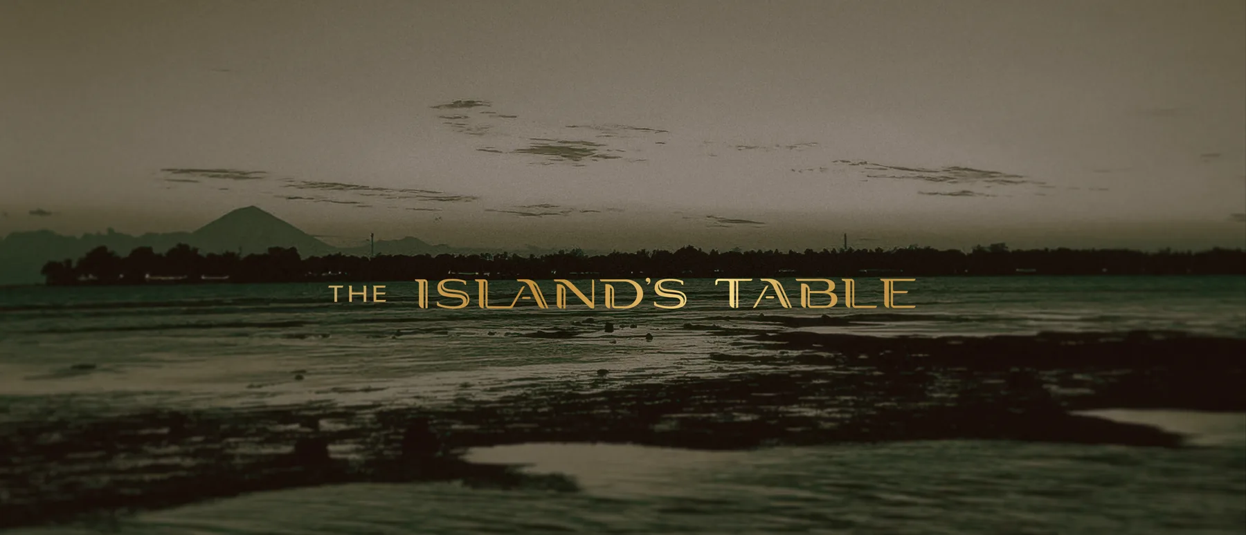 The Island’s Table wordmark over a dusk shoreline with bungalows on the water