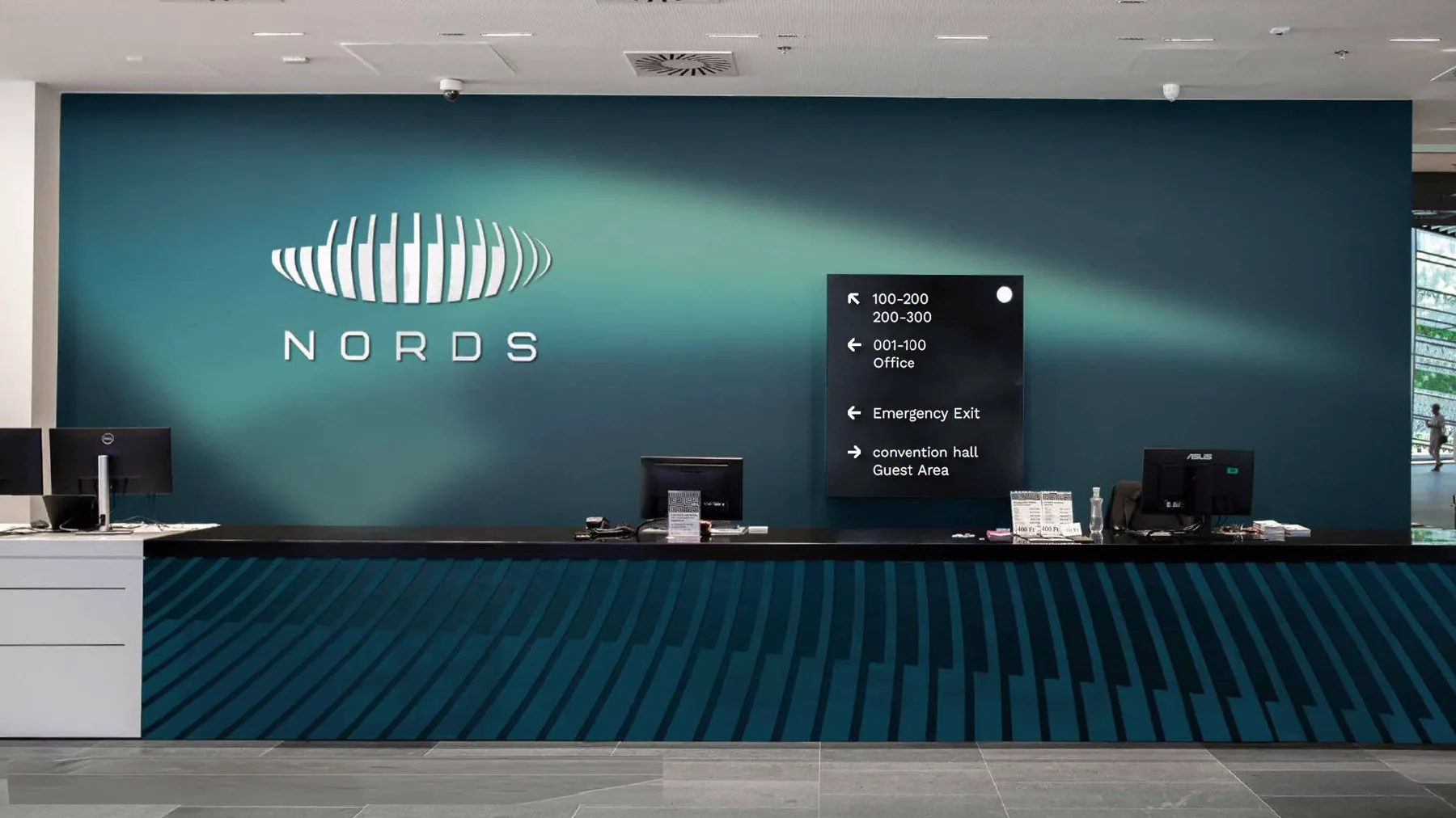 Reception wall with the Nords logo over an aurora-green gradient and a wayfinding sign