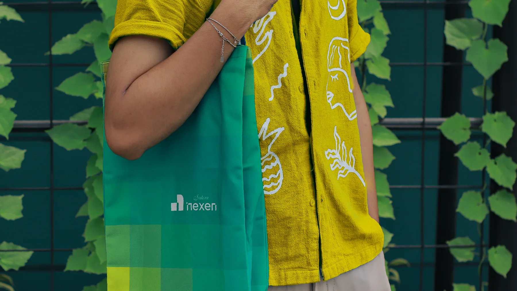 Teal Nexen tote bag held against a yellow patterned shirt