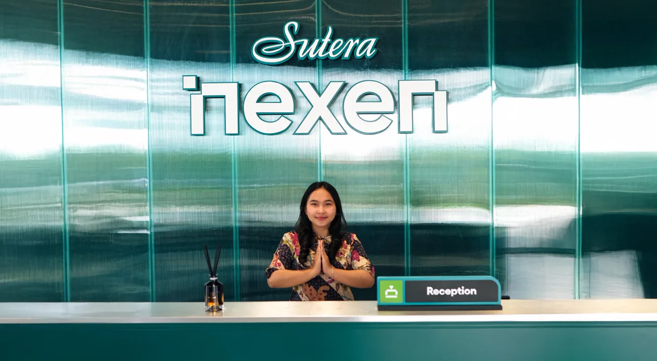 Receptionist with her hands pressed together behind a teal desk under the glass-clad Nexen logo wall
