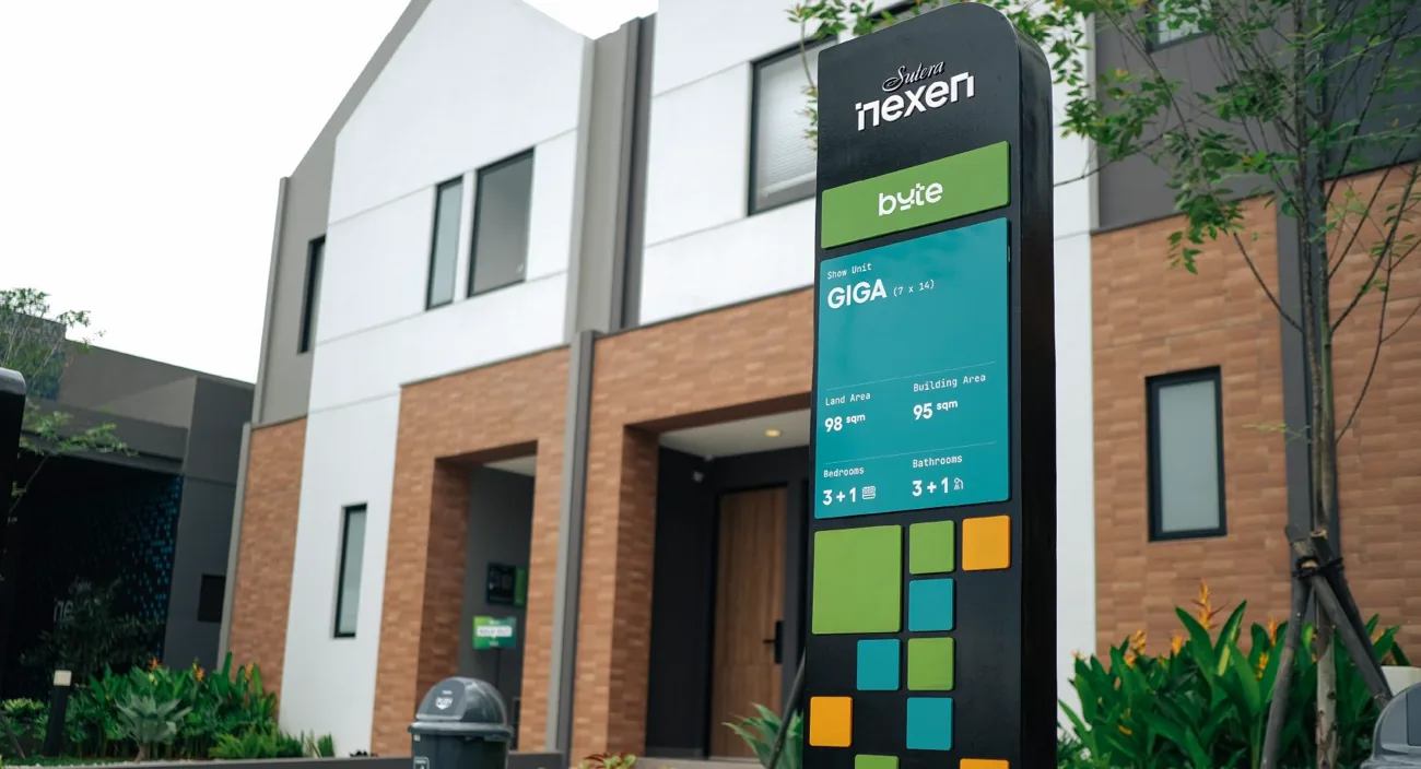 Black unit-information totem with a green byte plate reading GIGA, in front of a brick-and-white townhouse