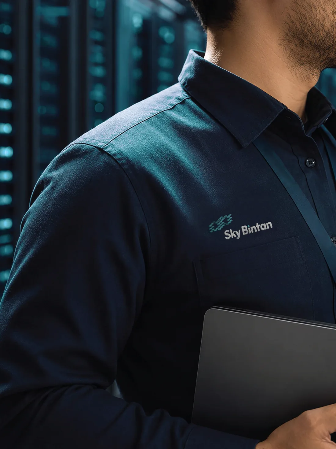 Technician in a navy uniform with the Sky Bintan logo on the chest, holding a tablet in front of server racks