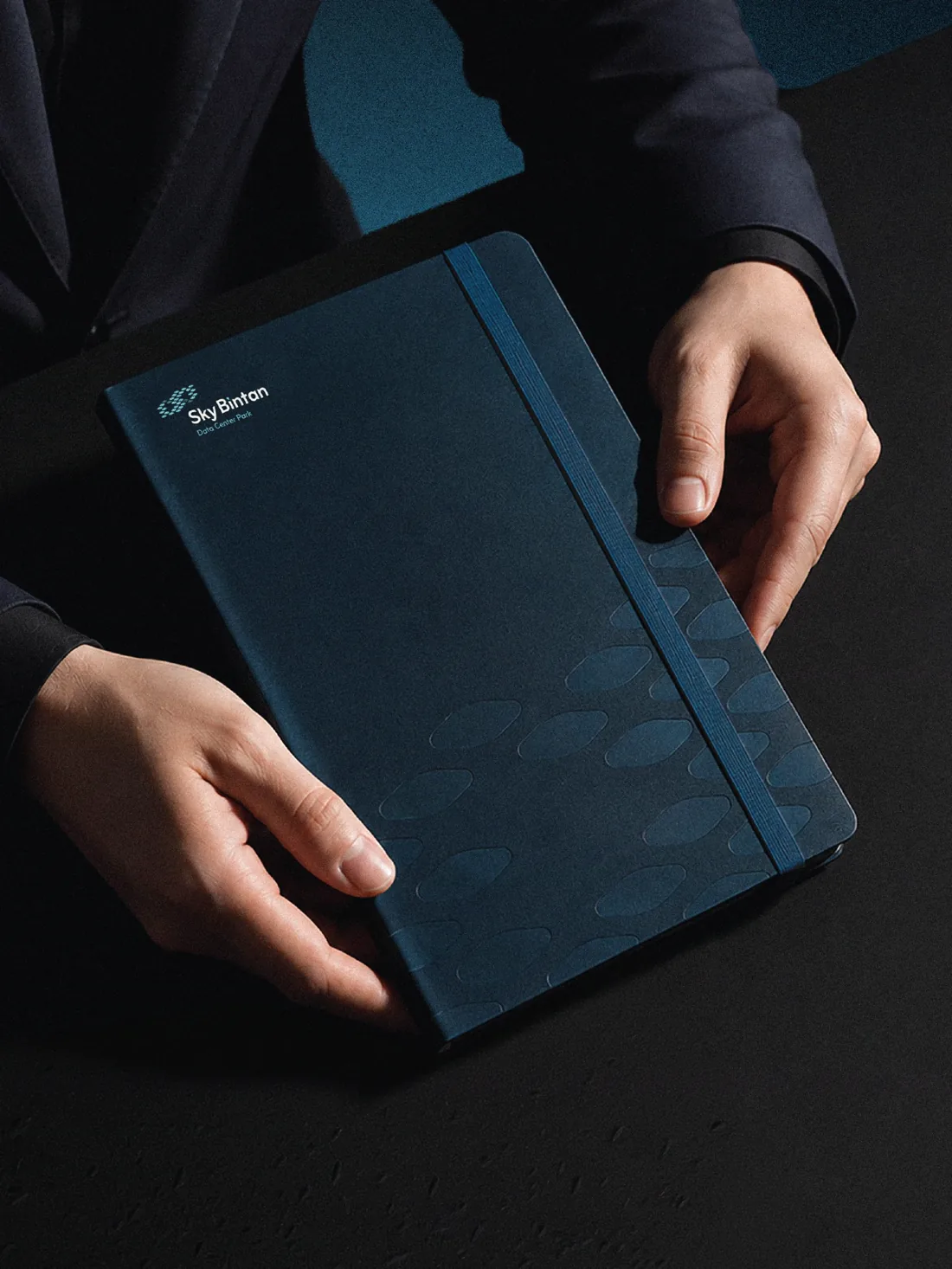 Hands holding a teal Sky Bintan notebook with a pixel pattern