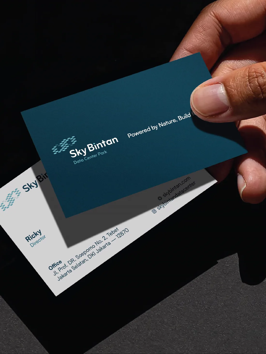 A hand holding a teal Sky Bintan business card above a printed card